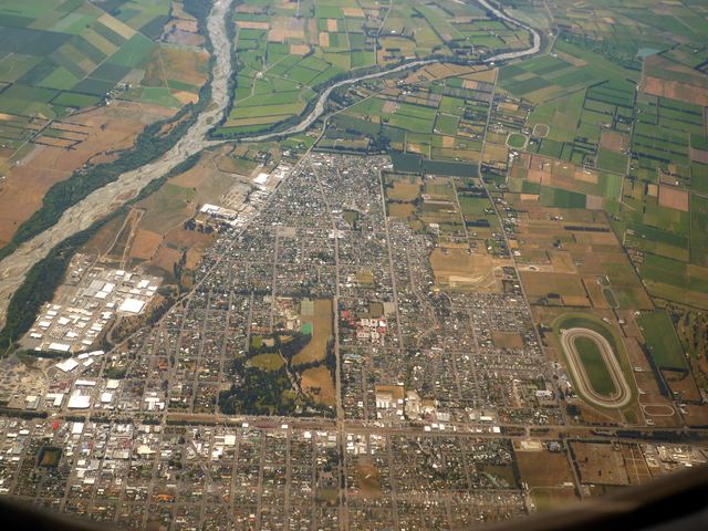 Aerial view of Ashburton's grid of streets beside the braided Ashburton River, with farmland beyond.