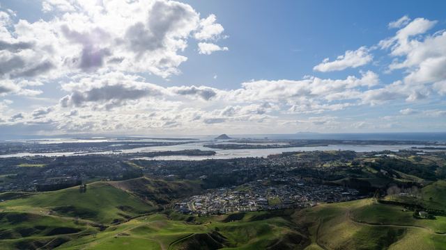 Aerial view of Tauranga with the harbour, coastline and hills under a bright sky.