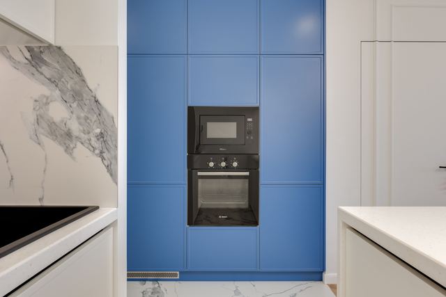 A built-in wall oven with a microwave above it, set into a tall run of blue kitchen cabinets.