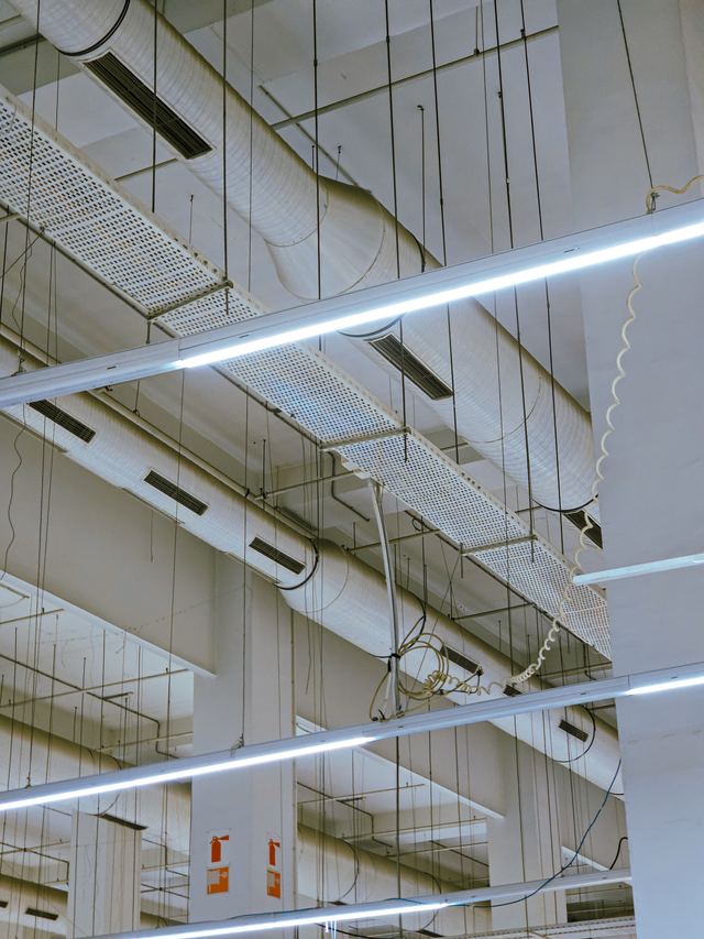 A commercial ceiling with suspended LED batten lights, a cable tray and air-conditioning ducts.