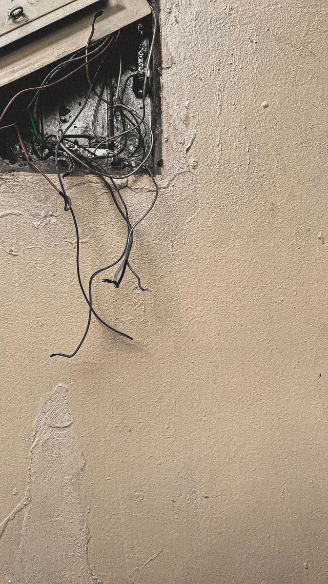 Old frayed wires hanging out of an open box in a cracked plaster wall.