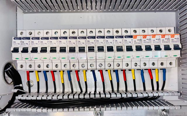 A row of circuit breakers marked 240/415 V with red, yellow and blue sleeved cables below, inside a grey metal panel.