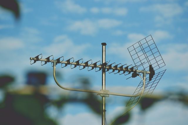 A rooftop TV aerial with a long row of looped elements and a mesh reflector, against a blue sky with soft clouds.